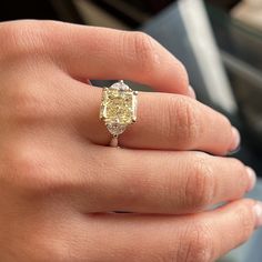 a close up of a person's hand wearing a ring with a yellow diamond