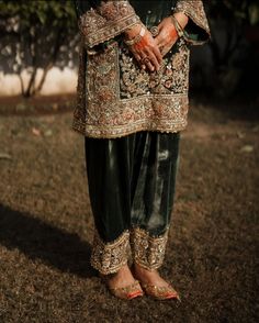 a woman standing in the grass with her hands on her hips and wearing green pants