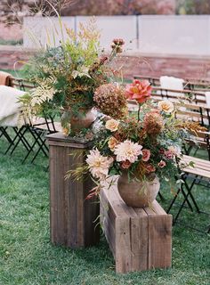 an arrangement of flowers and greenery in vases sitting on wooden stools outside