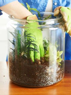 a person wearing green gloves and gardening gloves in a jar filled with dirt and plants