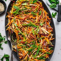 a black plate topped with carrots and green beans next to silverware on a white table