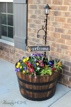 a welcome sign sitting on top of a barrel filled with flowers