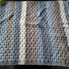 a crocheted blanket sitting on top of a wooden table next to a green plant