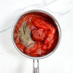 a bowl filled with red sauce and seasoning sitting on top of a white counter