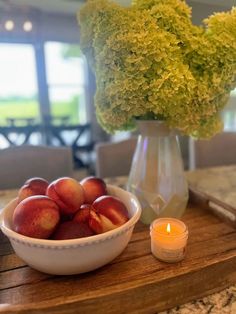 a white bowl filled with peaches on top of a wooden table next to a candle