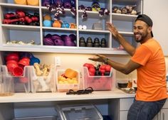 a man in an orange shirt standing next to a shelf filled with plastic bins