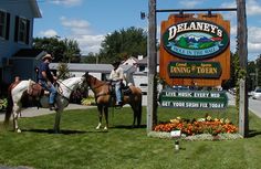 two people riding horses next to a sign for delany's in the town