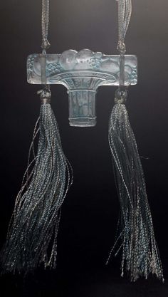 a glass sculpture with tassels hanging from it's sides on a black background