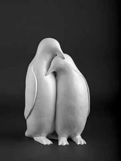 two white ceramic penguins standing next to each other on a black background with one holding the other's head