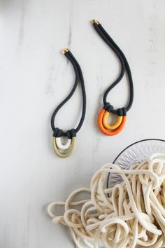 two necklaces that are sitting on top of a white table next to some noodles