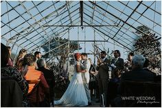 a bride and groom standing in front of an audience at a wedding ceremony under a glass roof