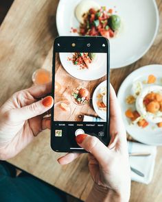 a person holding up a cell phone to take a picture of food on the table