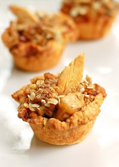 three small pies on a white plate with nuts and other toppings in the background