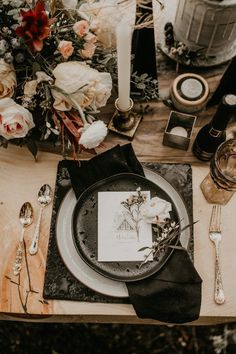 the table is set with black and white plates, silverware, flowers and candles