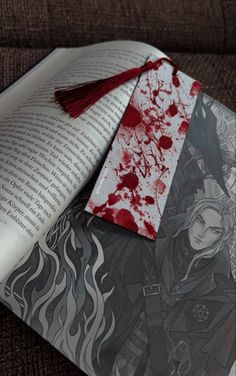 an open book with blood on the pages and a red tassel hanging from it