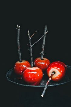 four red apples on a black plate with sticks