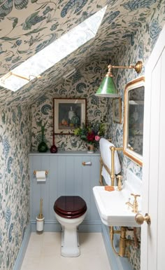 a bathroom with a toilet and sink under a skylight next to a wallpapered wall