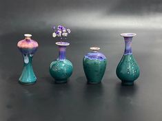 five vases are lined up on a black surface with flowers in the middle and one is blue