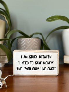 a wooden sign that says i am stuck between i need to save money and you only live once