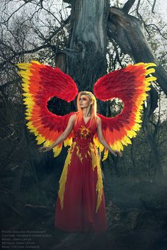 a woman with red and yellow wings standing in front of a tree