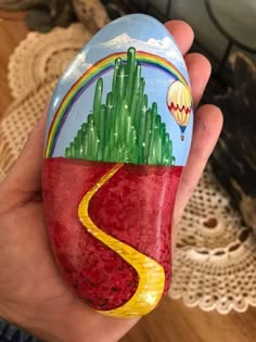 a hand holding an easter egg painted with a painting of a road leading to a cactus