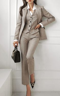 a woman in a suit leaning against a wall with her hand on her hip and holding a purse