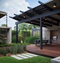 an outdoor patio with wooden decking and black pergolated roof, surrounded by green grass