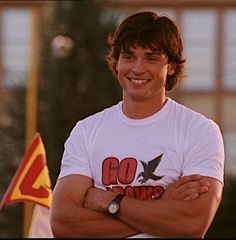 a young man standing with his arms crossed in front of two flags and a building