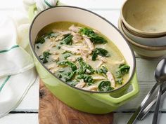 a green pot filled with chicken and spinach on top of a wooden cutting board