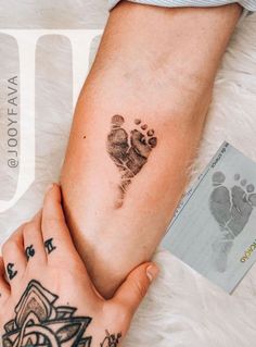 two people holding hands with small tattoos on their arm and foot prints in the middle