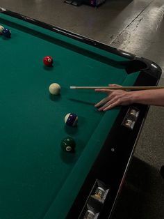 a pool table with several billiards on it and one person reaching for the ball