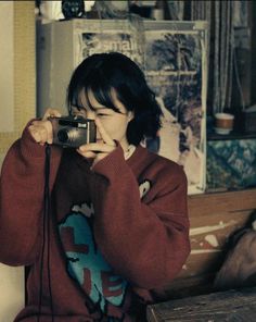 a woman holding a camera up to her face while sitting on a bench in front of a window