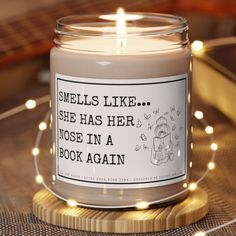 a candle that is sitting on top of a wooden table with lights around it and the words smells like she has her nose in a book again