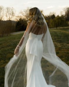 a woman in a white wedding dress is walking through the grass with her veil flying