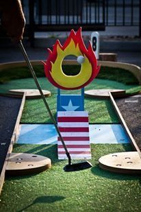 a miniature golf course with an american flag on it and a fire in the middle