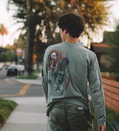 a man is walking down the sidewalk with his skateboard in hand and wearing a skull shirt