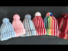 five knitted hats are lined up on a gray surface, one is multicolored and the other has pom - poms