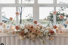 a table with flowers and candles on it in front of a large window at a wedding