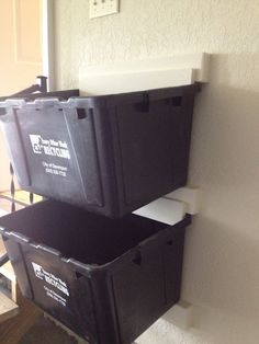 two black plastic storage bins sitting on top of a wooden floor next to a white wall