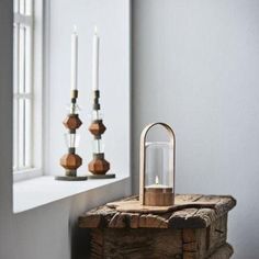 a wooden table topped with a lantern next to a window and two candles on top of it