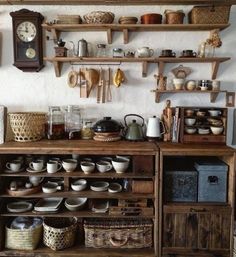 an old fashioned kitchen with lots of bowls and plates on the shelves, including a clock