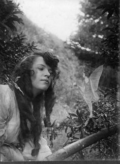 an old photo of a woman with long hair sitting in the grass next to trees