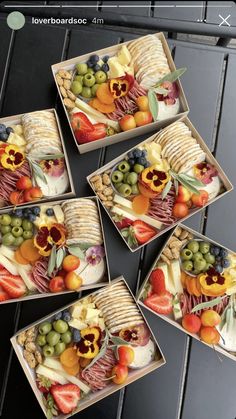 four square trays filled with assorted fruits and crackers on top of a table