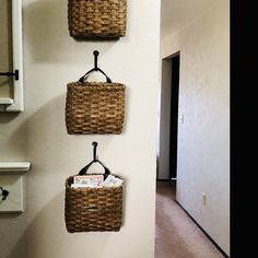 three wicker baskets hanging on the wall in a hallway next to a toilet paper dispenser