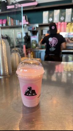 a pink drink sitting on top of a metal counter next to a person in a black shirt