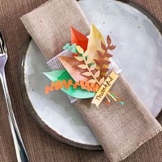 a place setting with napkins and silverware on a plate, decorated with autumn leaves