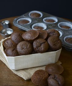 chocolate muffins in a paper container on a table next to cupcake tins