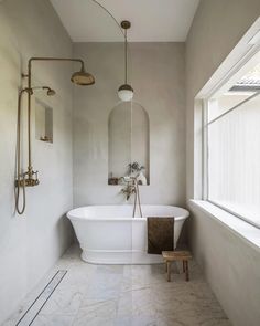 a white bath tub sitting under a window next to a wooden stool in a bathroom