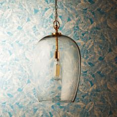 a clear glass light fixture hanging from a chain on a blue and white wallpapered background