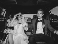 a man and woman sitting in the back of a car, dressed in formal wear